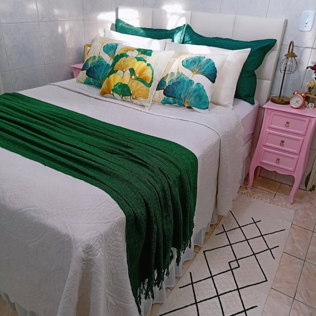 Quarto de casal com roupa de cama branca, manta verde, almofadas com flores e fronhas verdes
