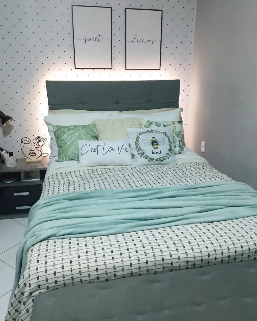 Quarto de casal com cama posta em tons de verde, papel de parede branco com bolinhas pretas e quadros brancos