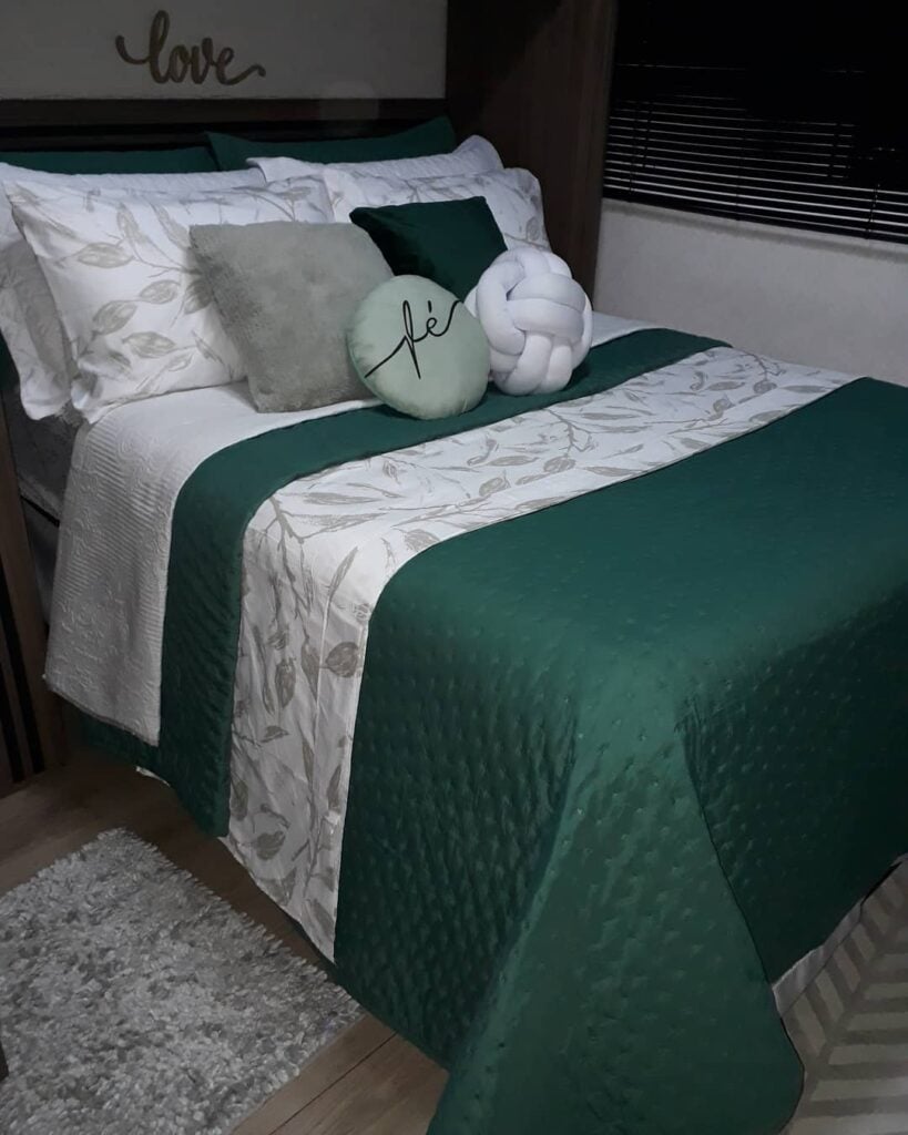 Quarto de casal com roupa de cama branca e verde e várias almofadas