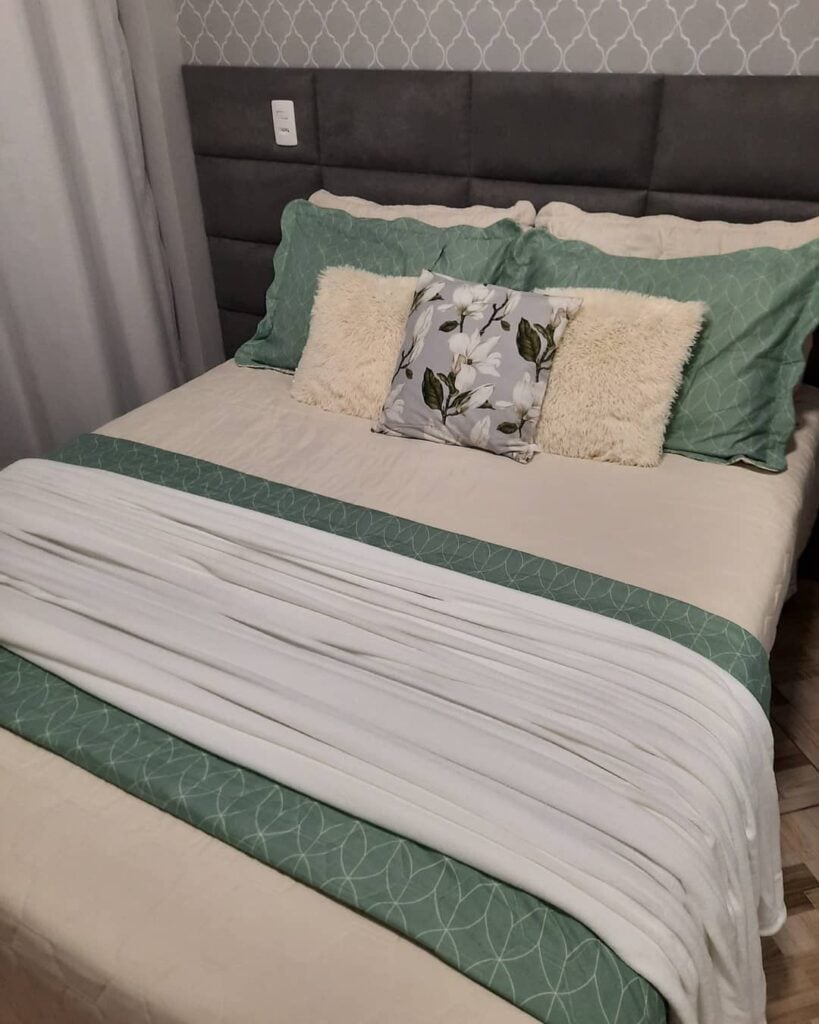 Cama com cabeceira cinza estofada em veludo com colcha e almofadas verde
