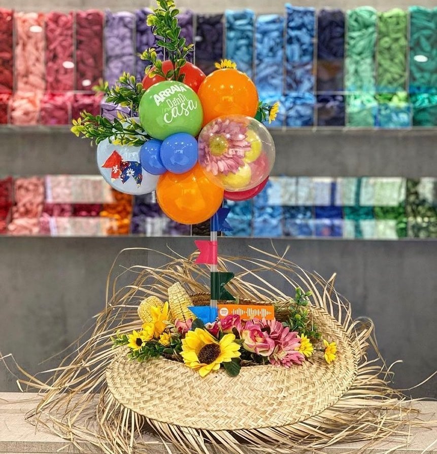 Chapéu de palha com a abertura para cima, decorado com balões, flores e doces