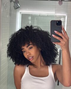 Mulher de pele preta, com regata branca e cabelo cacheado escuro