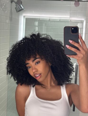 Mulher de pele preta, com regata branca e cabelo cacheado escuro