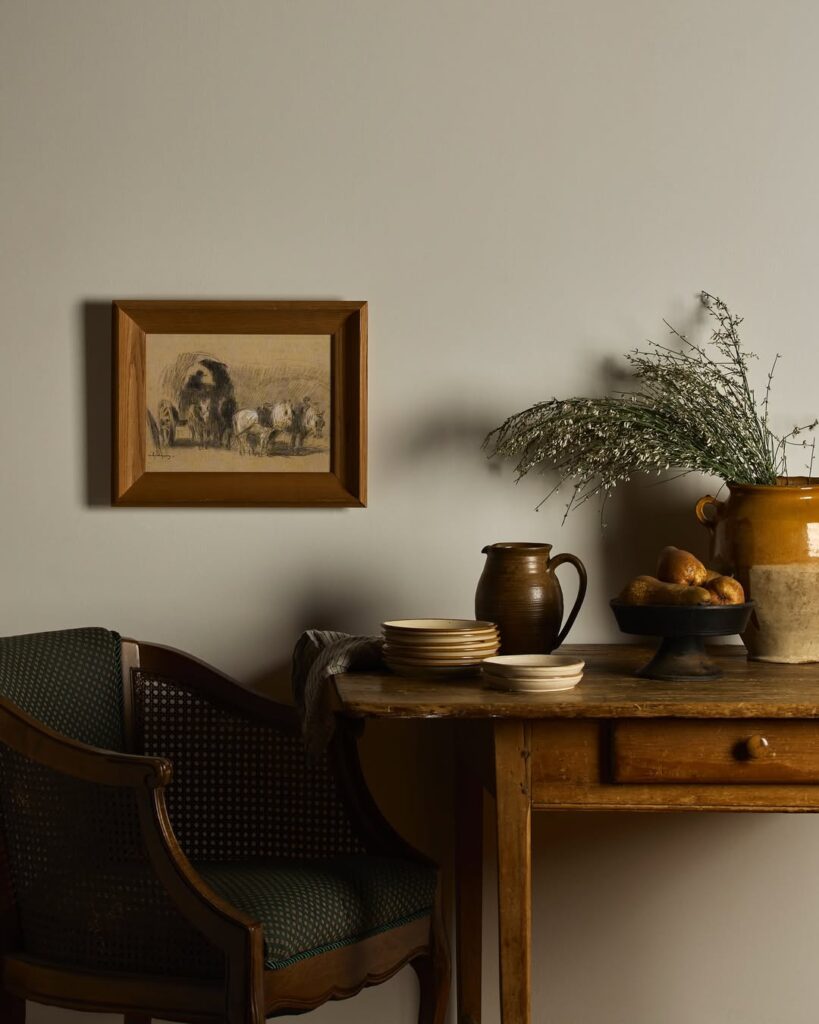 Mesa de madeira com gaveta, pratinhos e jarros, ao lado de uma cadeira antiga