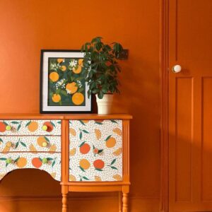Parede laranja com aparador na mesma cor e papel de parede com frutas