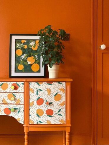 Parede laranja com aparador na mesma cor e papel de parede com frutas