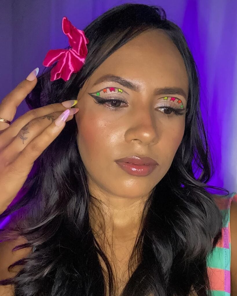 Mulher de pele preta, com blusa estampada, cabelo escuro com laço e maquiagem com delineado de bandeirinha