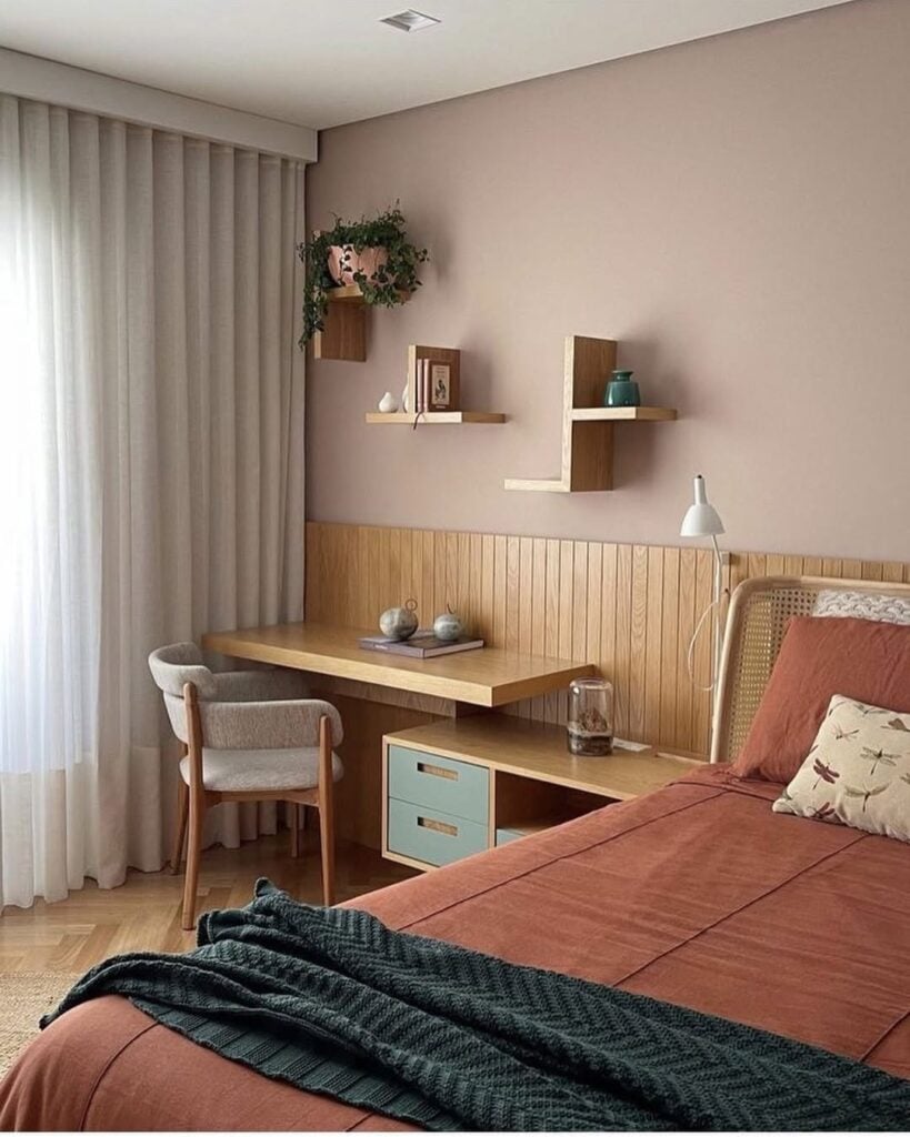 Quarto com painel amadeirado atrás da cama, escrivaninha minimalista com poltrona