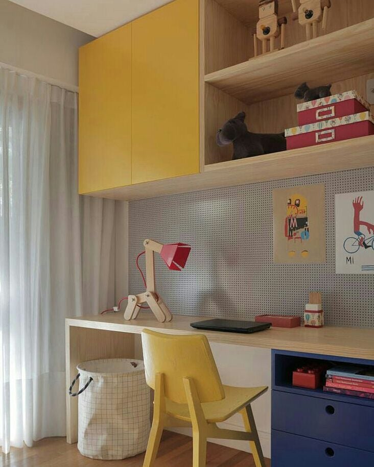 Quarto de criança com escrivaninha de madeira clara, gavetas azul-marinho e cadeira amarela