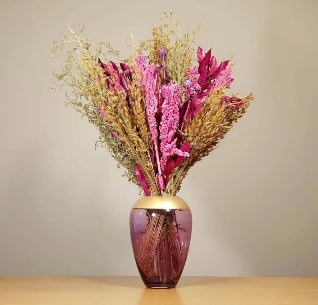 Vaso de vidro rosa e dourado com galhos secos bege e rosa