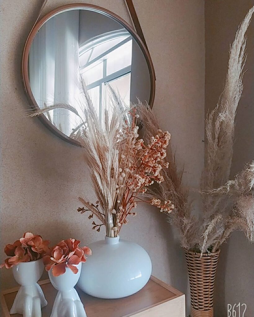 Vaso branco redondo com galhos e flores secas junto a um espelho Adnet