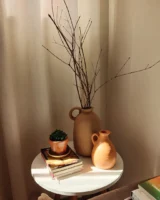 Mesa de canto branca com livros, jarro de barro com galhos secos
