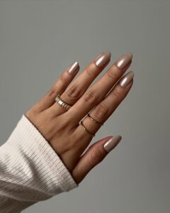 Mão de pele clara, com anéis em dourado e unha amendoada neutra e perolada