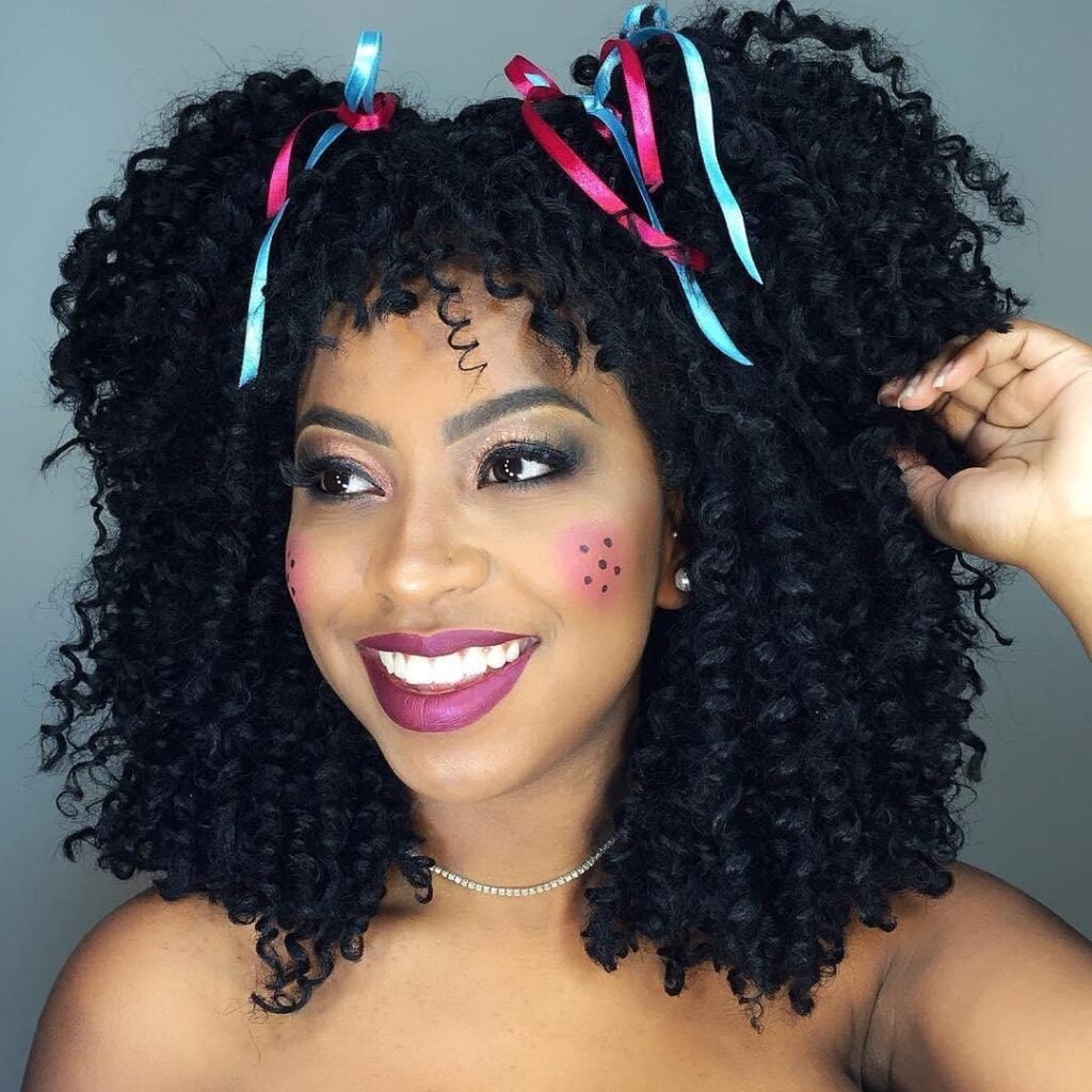 Mulher de pele preta, com cabelo escuro crespo com fitas e maquiagem de São João