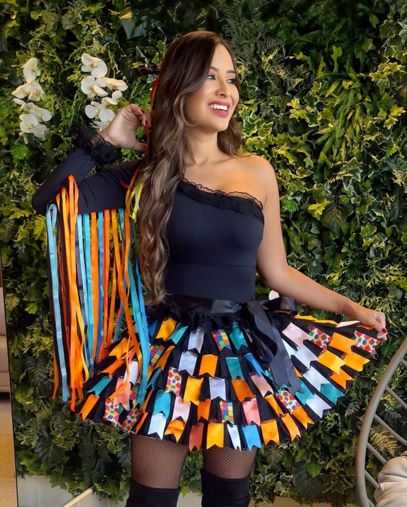 Mulher de pele clara, com blusa preta e saia preta com bandeirinhas coloridas