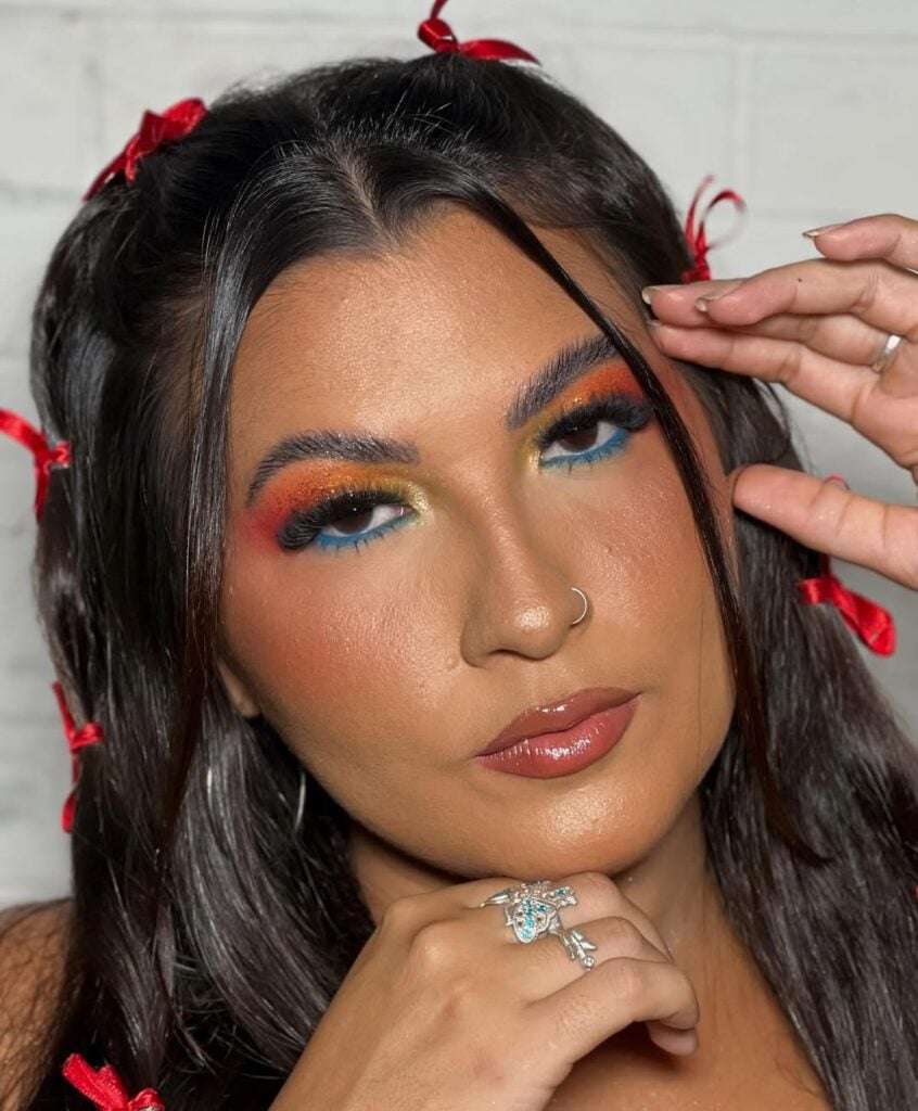 Mulher de pele preta-clara, com cabelo escuro meio preso com laços e maquiagem junina colorida