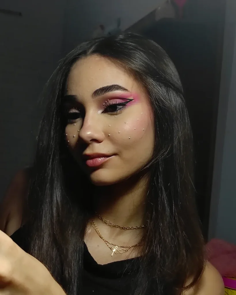 Mulher de pele clara, com blusa preta, cabelo escuro, acessórios em dourado e maquiagem de São João com pérolas
