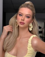 Mulher de pele clara, com blusa e acessórios amarelo-manteiga, cabelo loiro e maquiagem em tons rosados