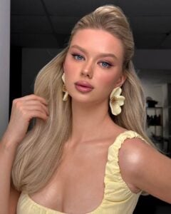 Mulher de pele clara, com blusa e acessórios amarelo-manteiga, cabelo loiro e maquiagem em tons rosados