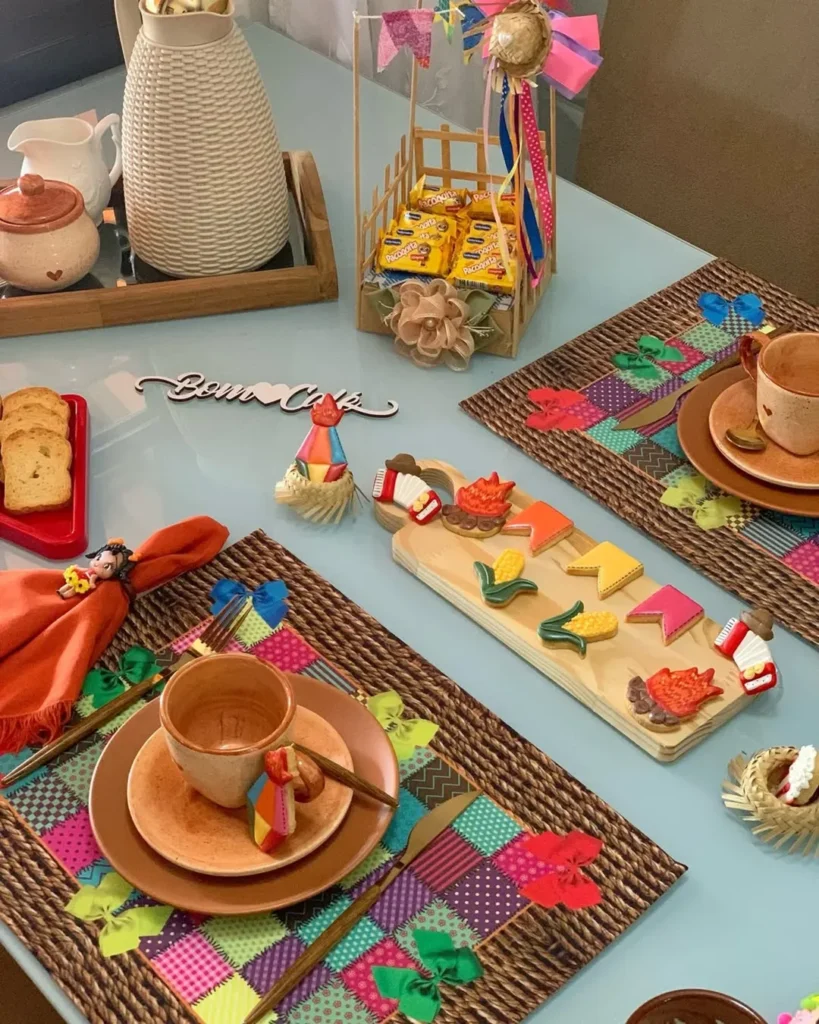 Mesa posta com jogo amaricano colorido, biscoitos em formato de bandeirinhas, milho e fogueira