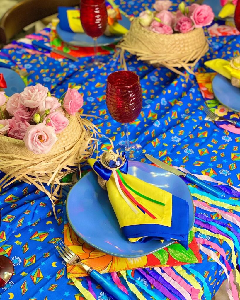 Mesa com tecido azul e balões juninos, chapéus de palha e guardanapos coloridos