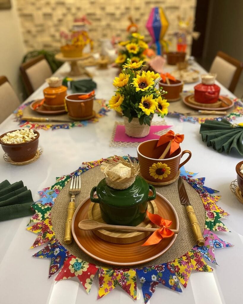 Mesa posta de São João com louças de cerâmica marrom, mini chapéus de palha e sousplat com bandeirinhas