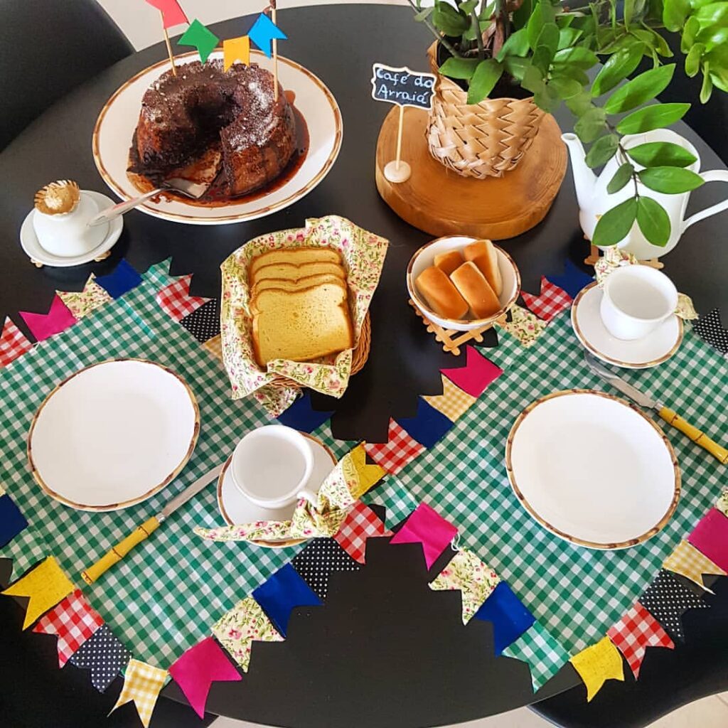 Mesa posta com jogo americano xadrez em branco e verde com bandeirinhas coloridas ao redor