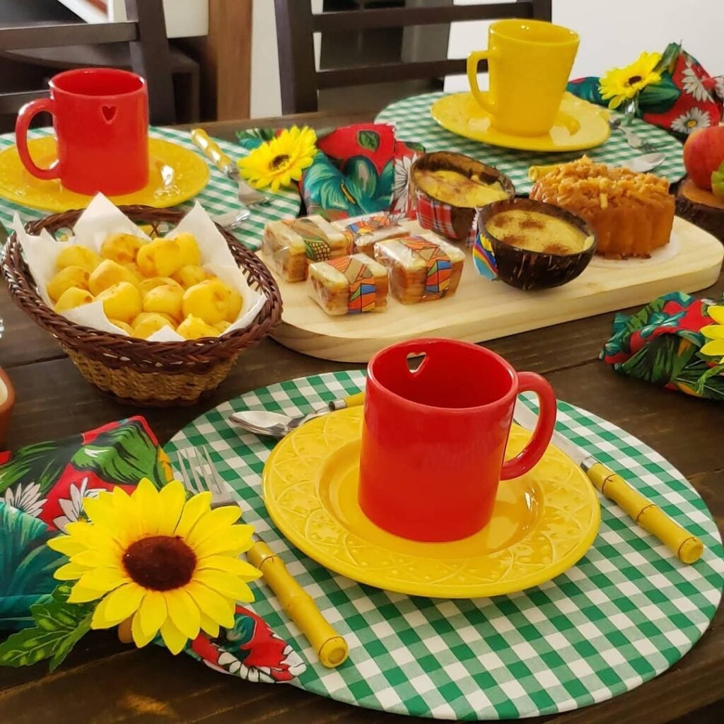 Mesa posta de São João com sousplat xadrez em verde e branco, pratinhos amarelos e canecas vermelhas