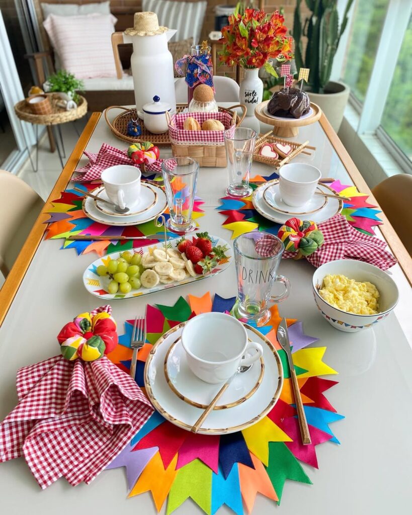 Mesa posta de café da manhã junino com frutas, sousplat com bandeirinahs e guardanapos xadrez em vermelho e branco