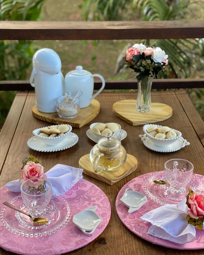 Mesa de madeira com sousplats rosa, xícara de vidro transparente, bandejas de bambu em formato de coração