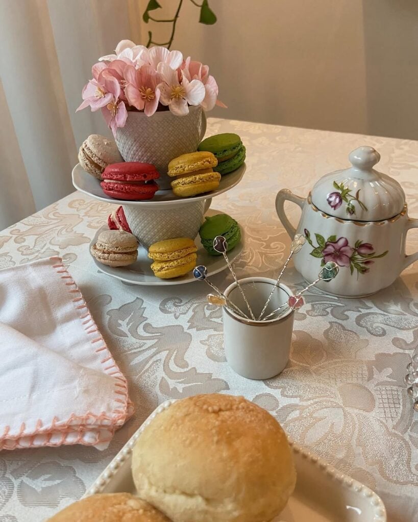Mesa com toalha branca, bule com flores, macarons e flores