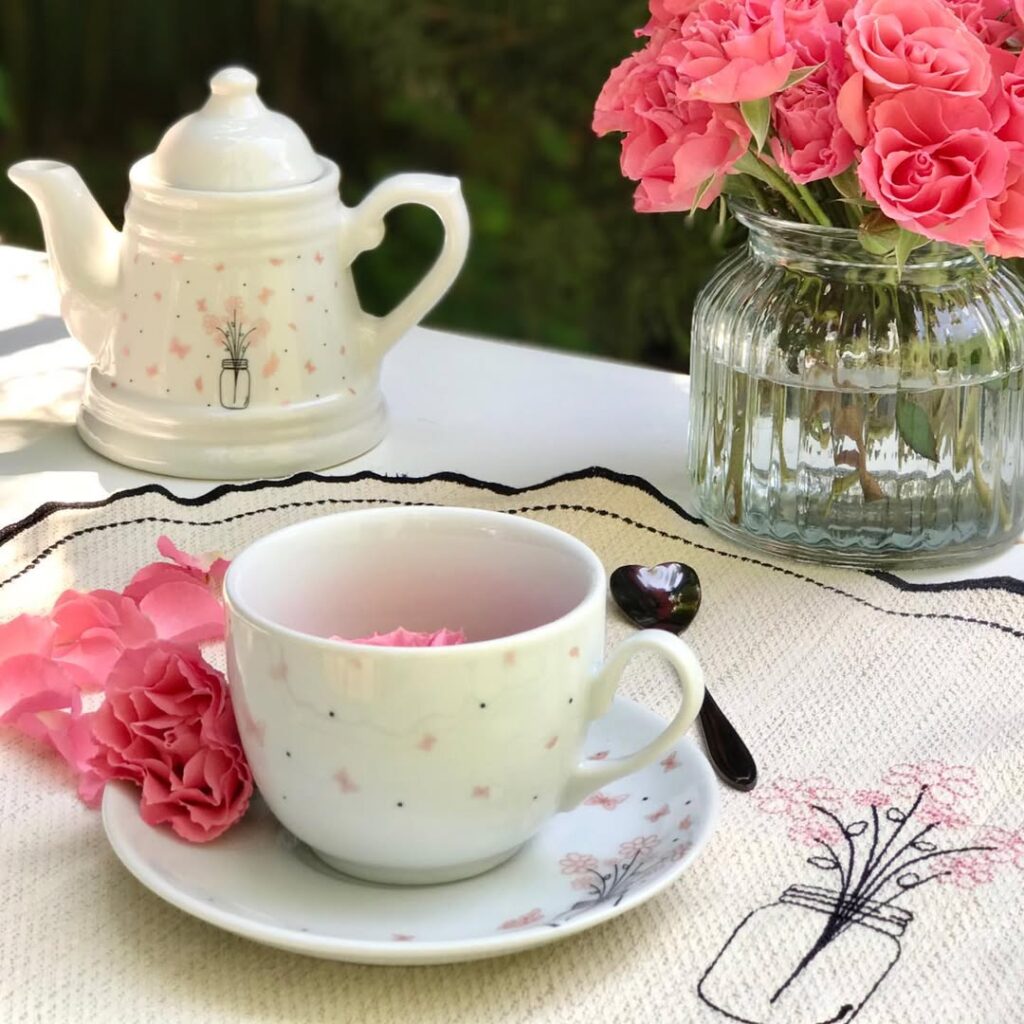 Mesa com jogo americano bege e borda preta, xícara e bule branco com bolinhas pretas e borboletas rosa