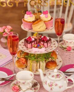 Mesa posta de chá com louças brancas e flores rosa, doces e salgados