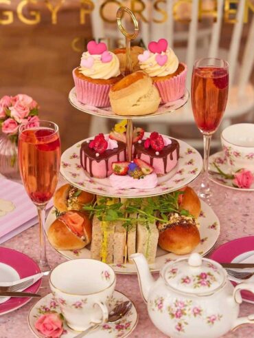 Mesa posta de chá com louças brancas e flores rosa, doces e salgados