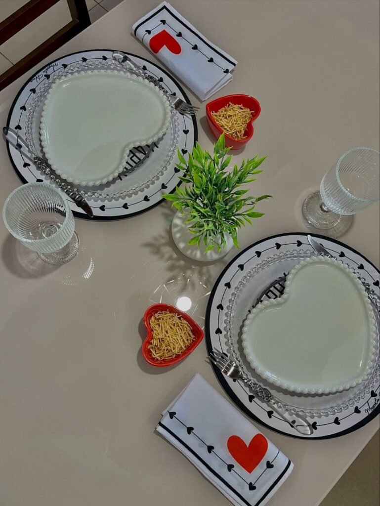 Mesa posta em branco e preto com sousplat com corações pretos, pratos brancos em formato de coração e guardanapo em vermelho, preto e branco