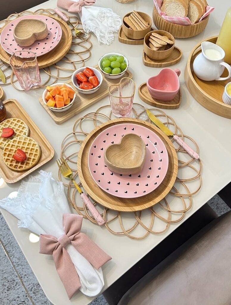 Mesa posta com itens de bambu , louças rosa e guardanapo branco com laço rosa