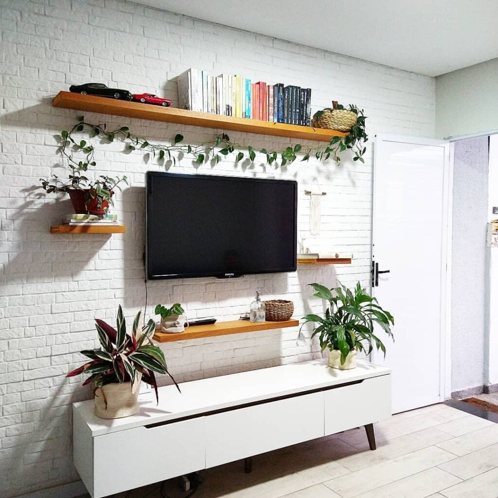 Sala de estar com parede de tijolinhos brancos prateleiras de madeira com livros e plantas