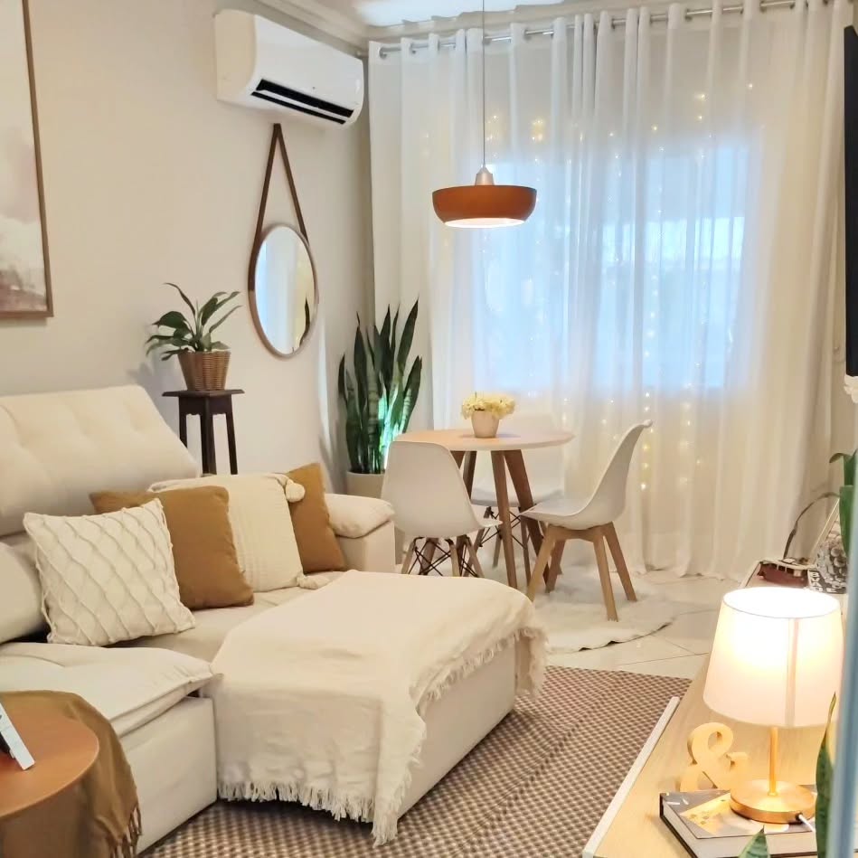 Sala em tons claros, sofá bege com almofadas e manta