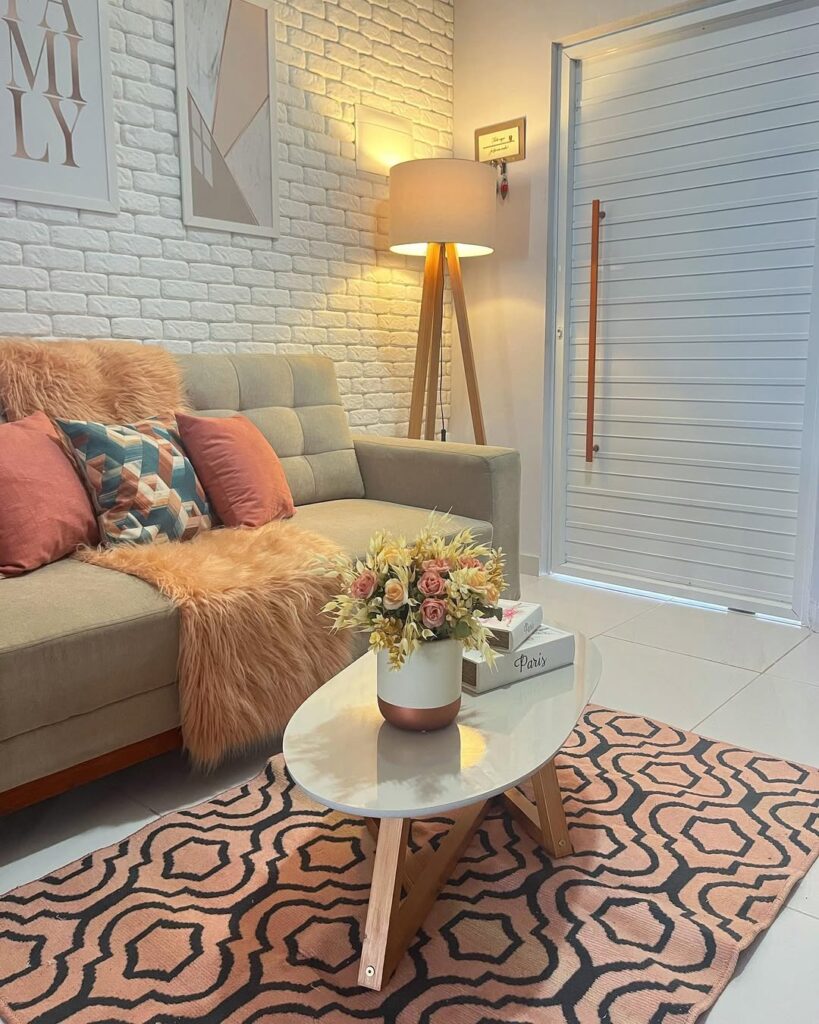 Sala com parede de tijolinhos, luminária de piso, porta pivotante e tapete em preto e marrom