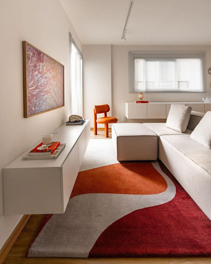Sala com paredes e sofá claro e tapete grande em bege, laranja e vermelho
