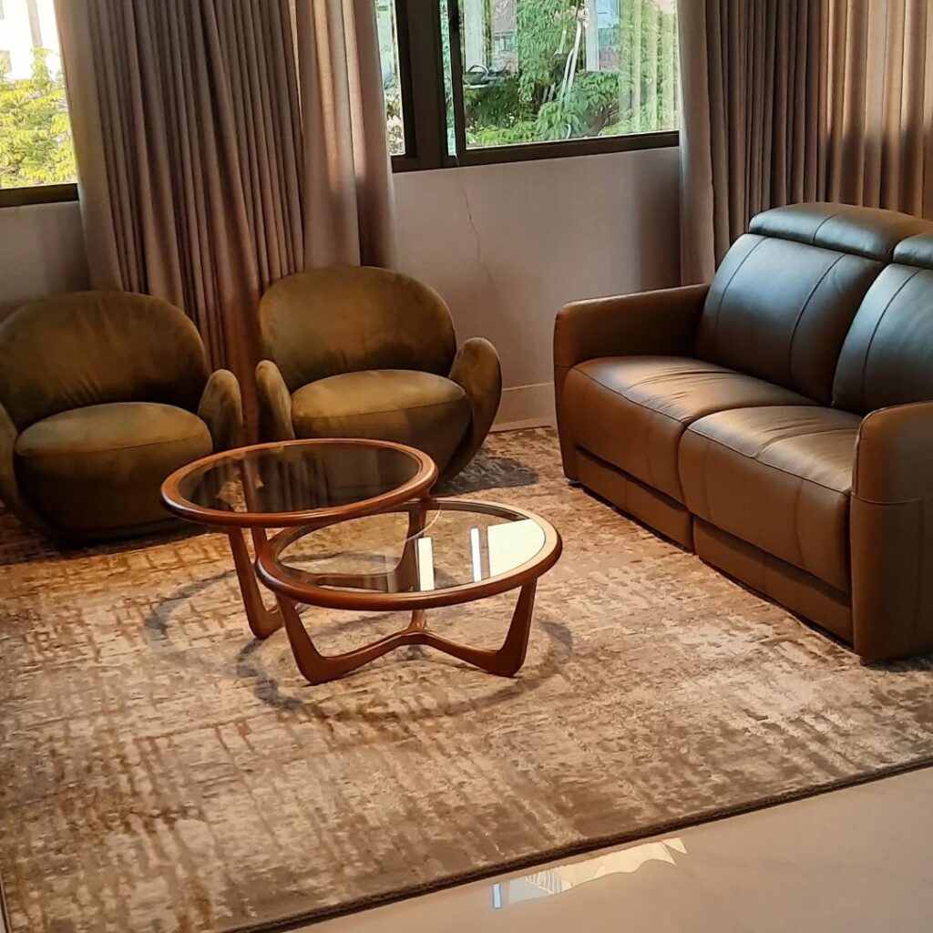 Sala de estar com sofá de couro marrom, duas poltronas, mesas de centro em madeira e vidro e tapete marrom