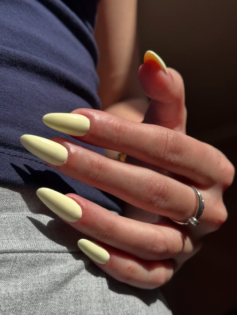 Mão de pele clara, com anel em prata e unha amendoada amarelo-manteiga 