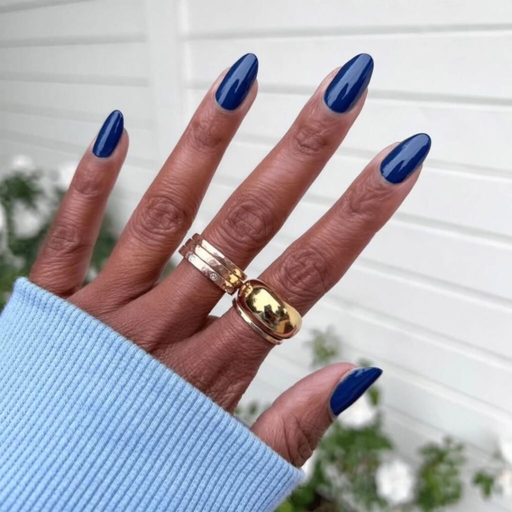 Mão de pele preta, com anéis em dourado e unha amendoada azul-marinho