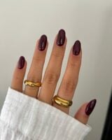 Mão de pele clara, com anéis em dourado e unha amendoada burgundy