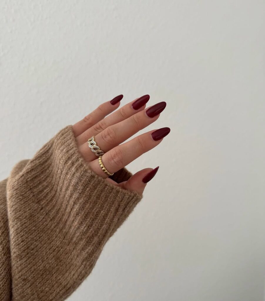 Mão de pele clara, com anéis em dourado e unha amendoada burgundy