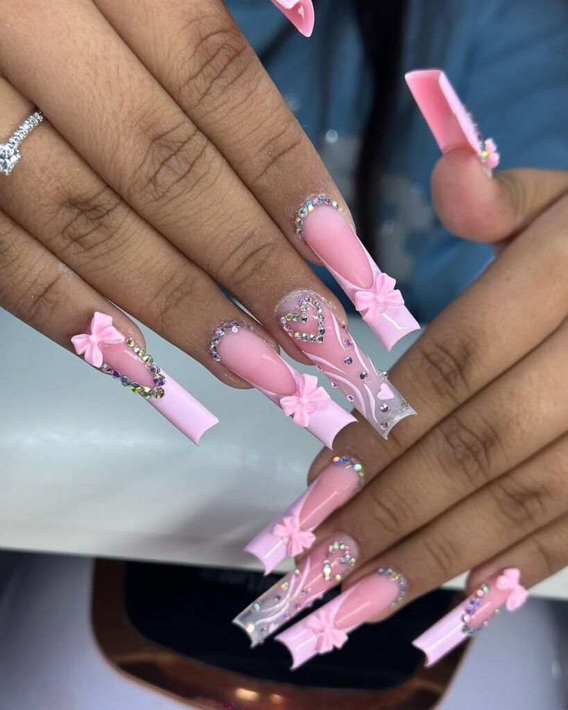 Mãos de pele preta, com unha quadrada com francesinha rosa-claro, laços e strasses