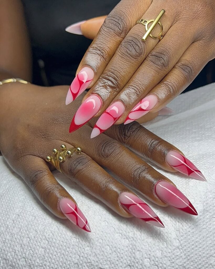 Mãos de pele preta, com anéis em dourado e unha amendoada com decorações em vermelho