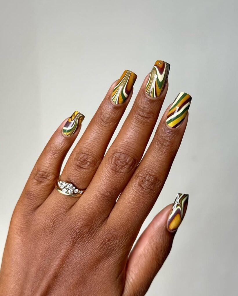 Mão de pele preta, com acessórios em dourado e unha quadrada estampada