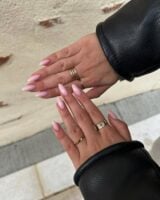 Mãos de pele clara, com anéis em dourado e unha amendoada rosa-claro