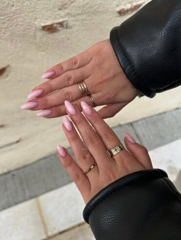 Mãos de pele clara, com anéis em dourado e unha amendoada rosa-claro